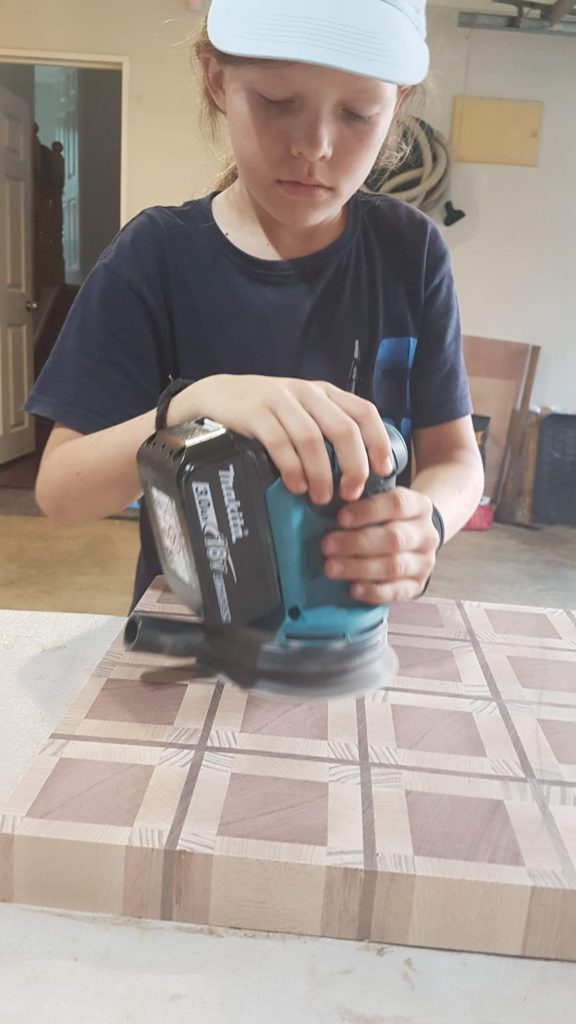 Home educated boy sanding woodwork with an electric sander